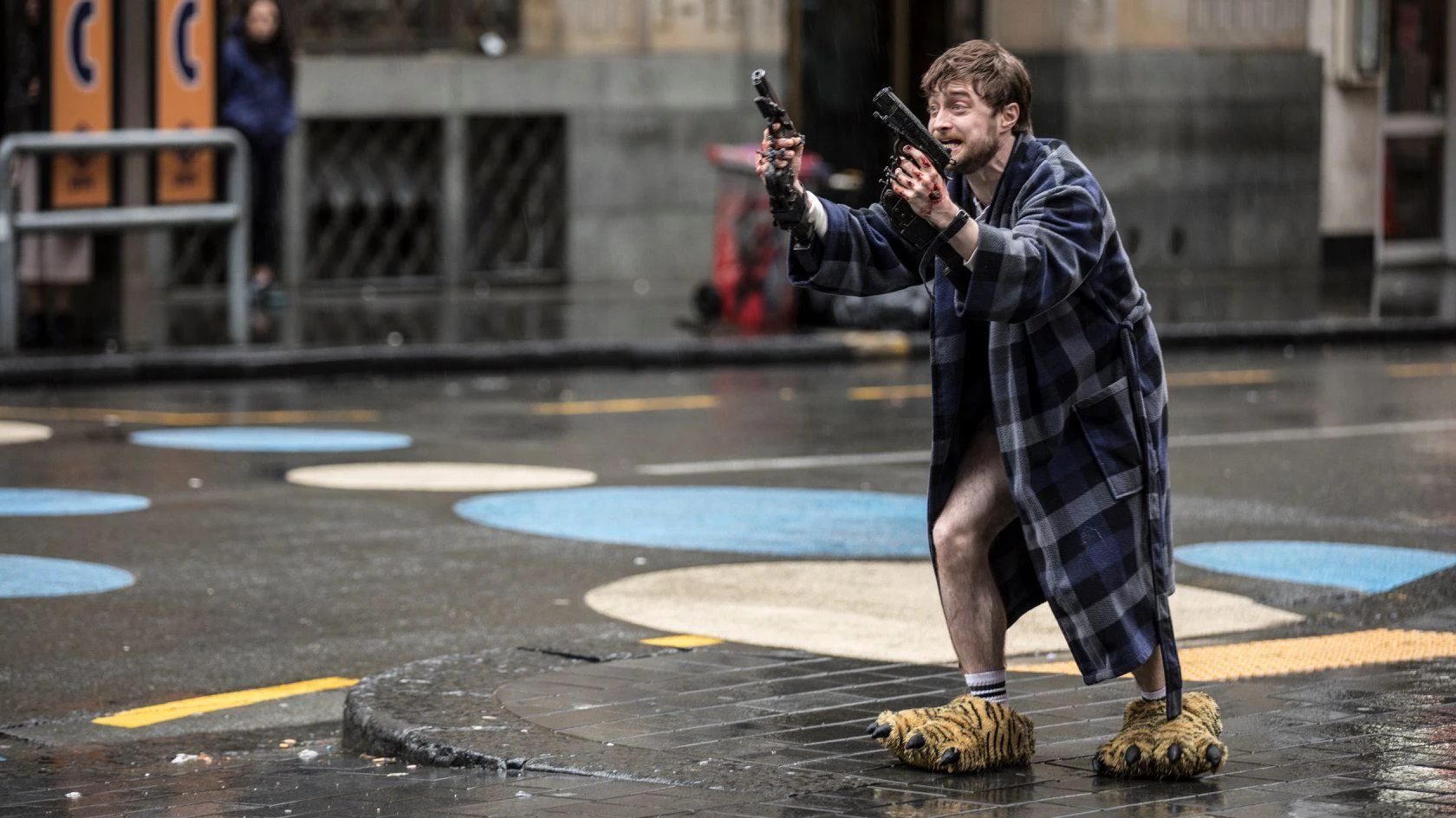 Fotograma de Guns Akimbo con Daniel Radcliffe en la calle vistiendo zapatillas de tigre, en ropa interior y bata de casa